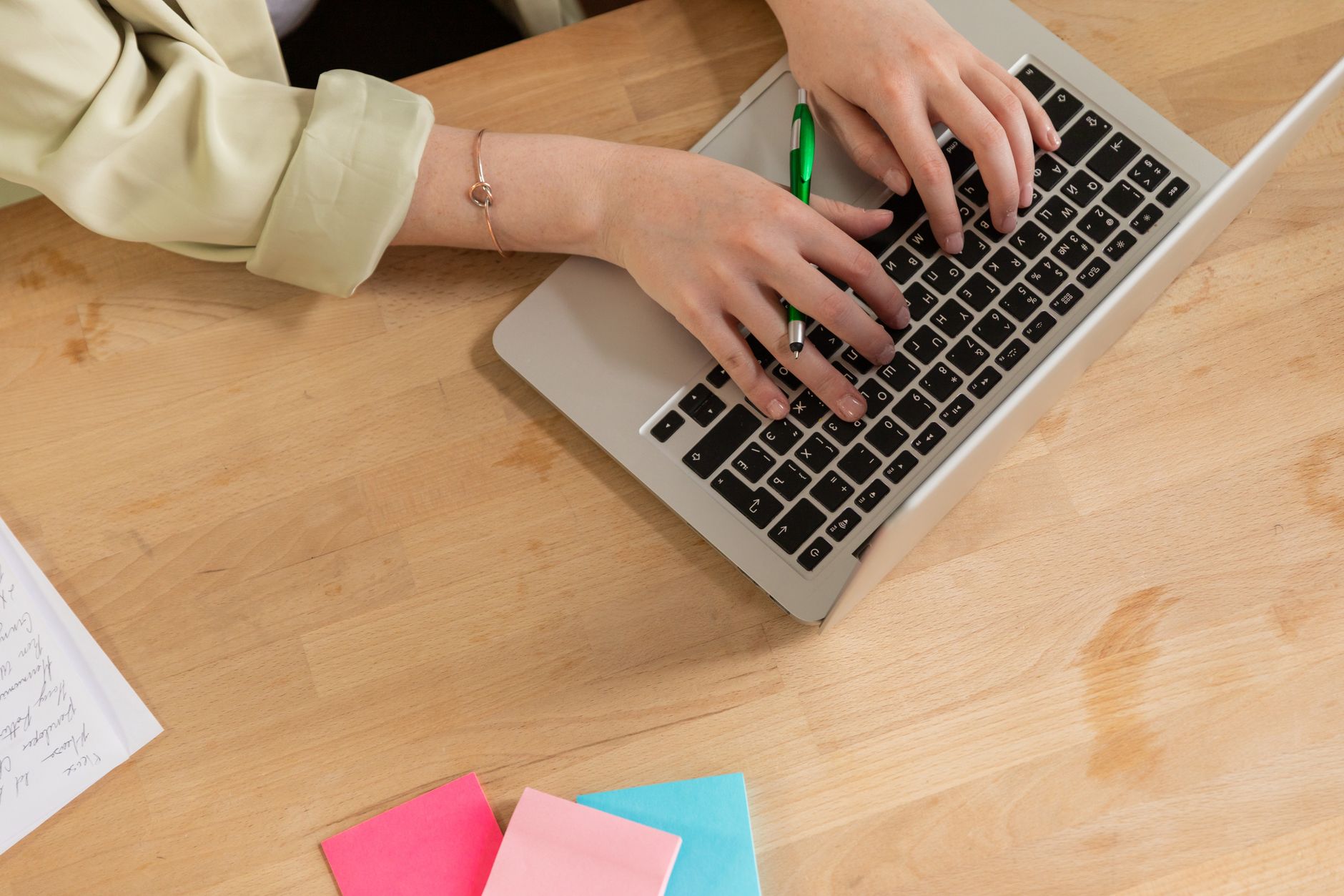 Hands typing on a laptop with a green pen and colorful sticky notes on a wooden desk — illustrating: How to Choose an Eco-Friendly Managed IT Provider in Central Florida Without Overpaying